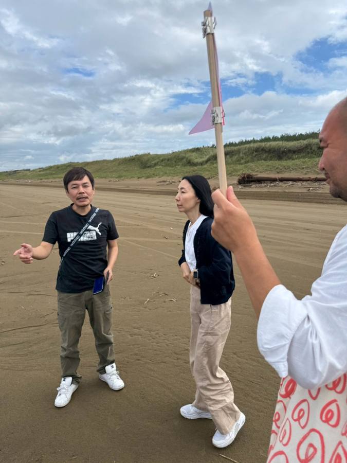 砂浜で旗を掲げ話す3人