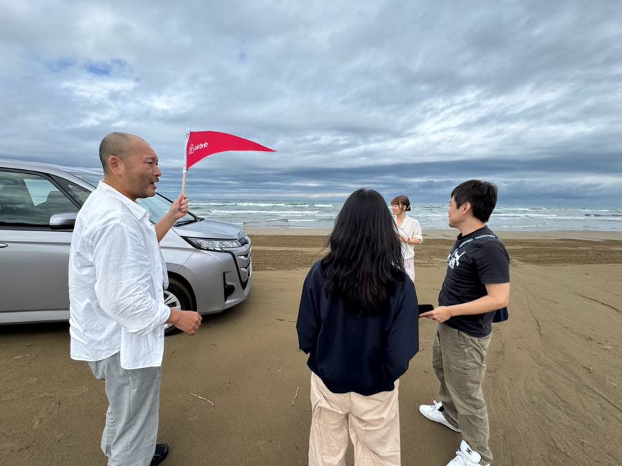 砂浜で車の前に立つ3人