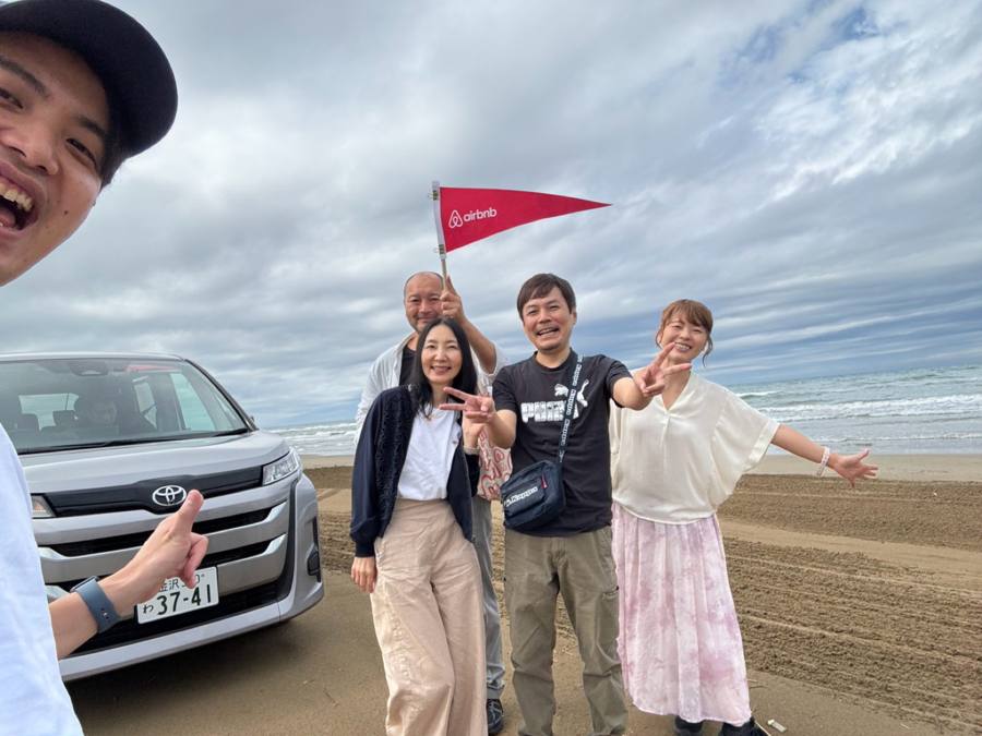 砂浜で旗を持つ4人の記念写真