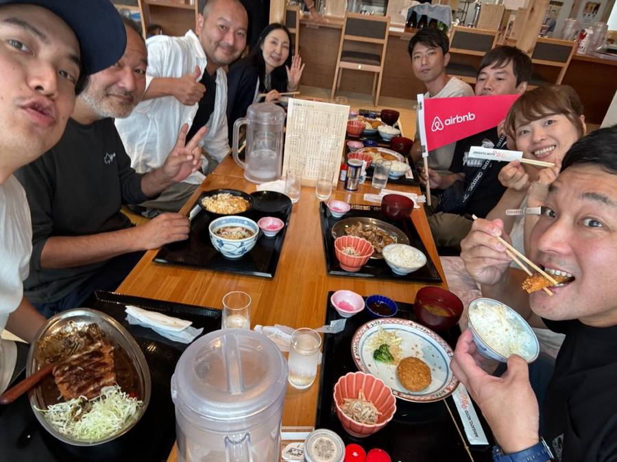 定食を前に旗を持ち笑う一行