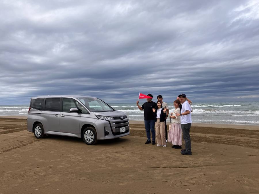 砂浜で車と記念撮影する一同